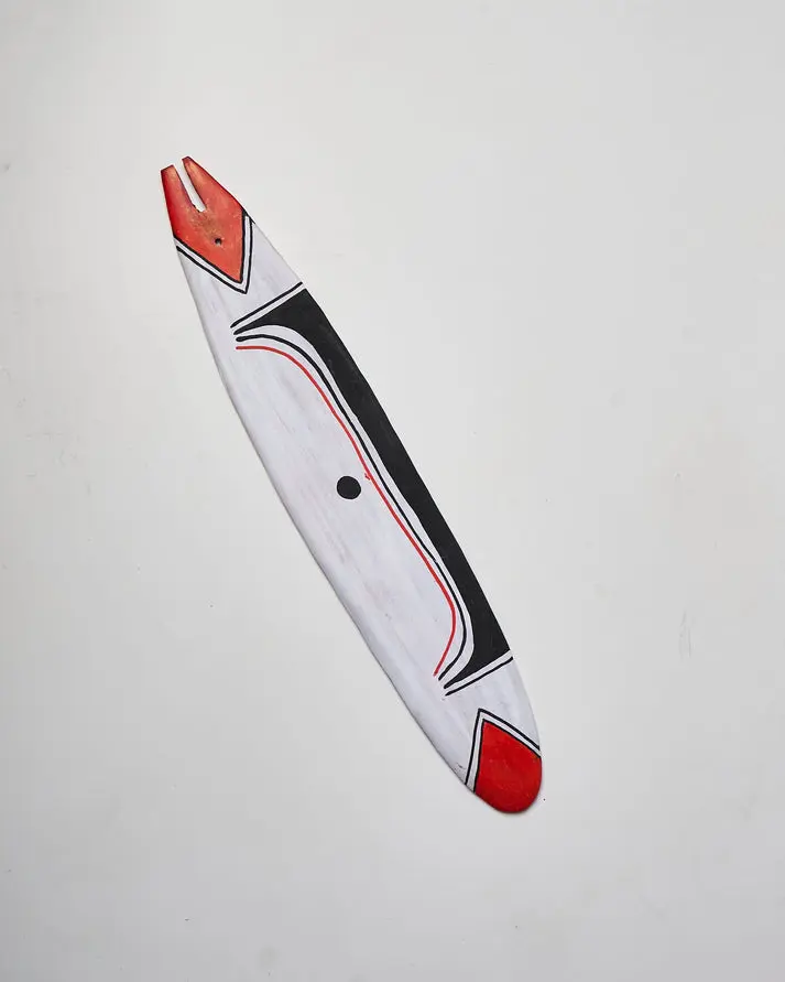 Lâmina alongada de madeira pintada de branco, com grafismos pretos e detalhes vermelhos nas extremidades.